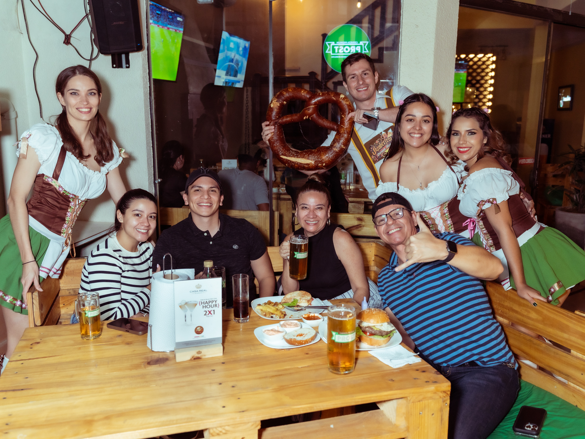 Clientes e animadoras de traje de Oktoberfest reunidos à mesa